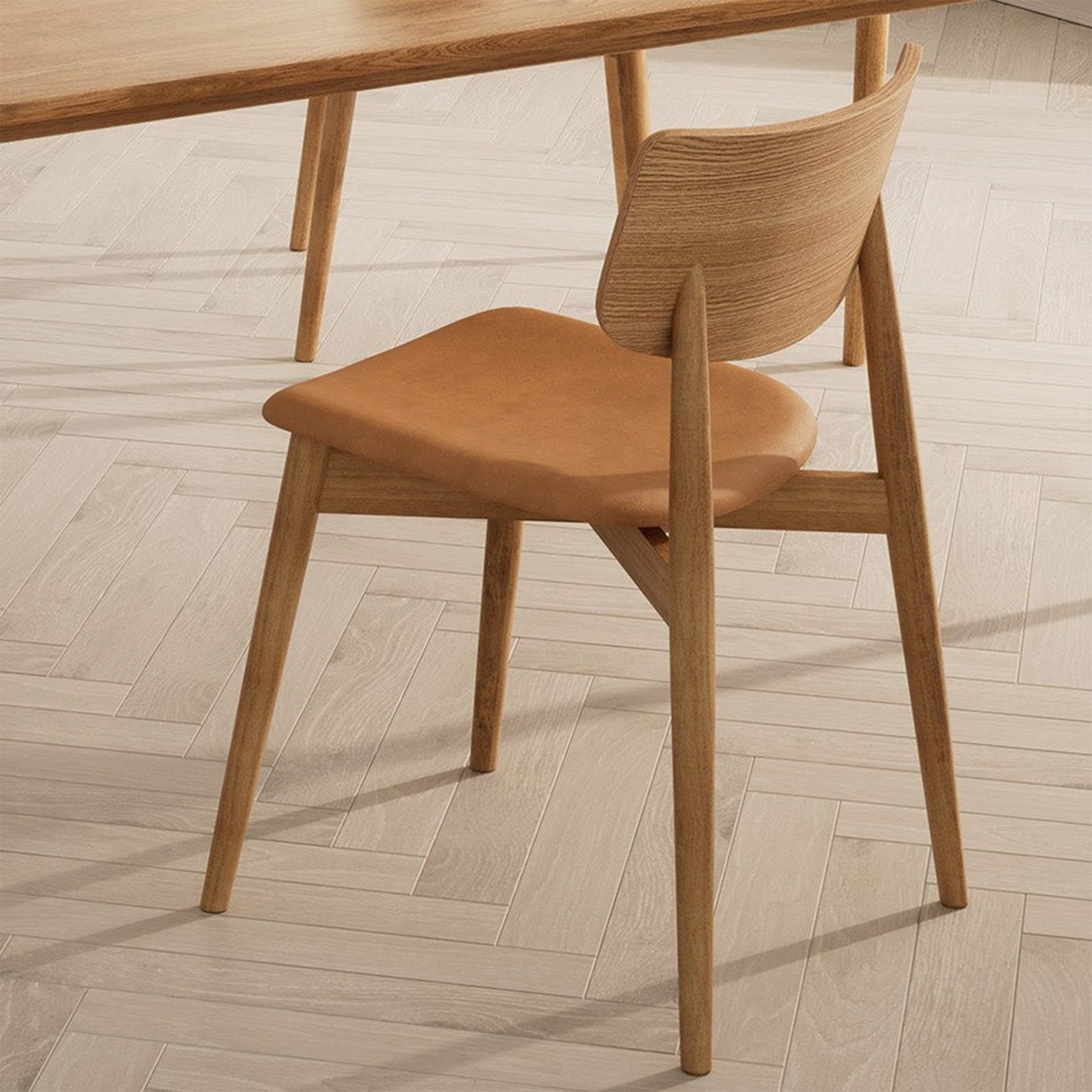 Bruunmunch Chiara chair in solid oak with natural oil finish and seat upholstered in brandy-colored aniline leather, showcased with the Bruunmunch Pure dining table, viewed from a slight rear angle on light herringbone parquet flooring