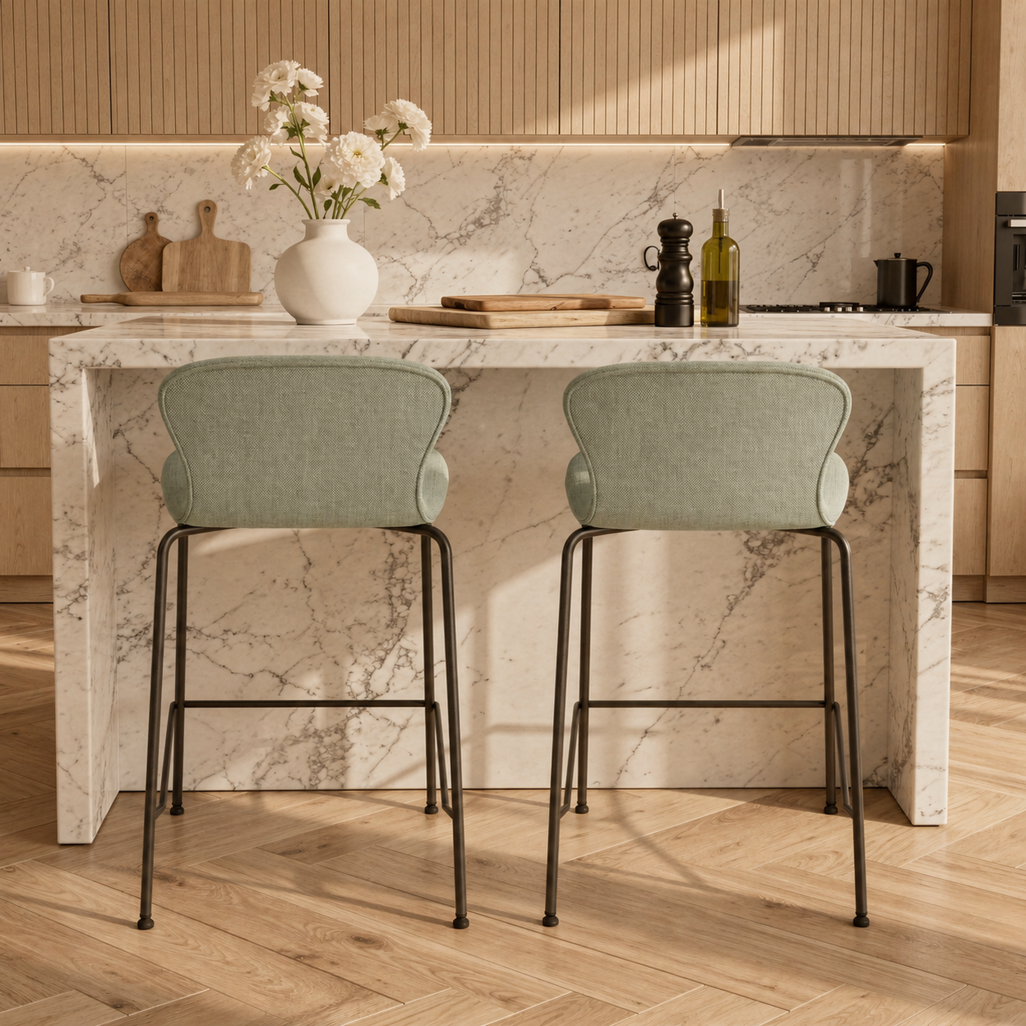 Two light sage green upholstered bar stools with black metal legs set at a kitchen island with a white marble countertop and backsplash.